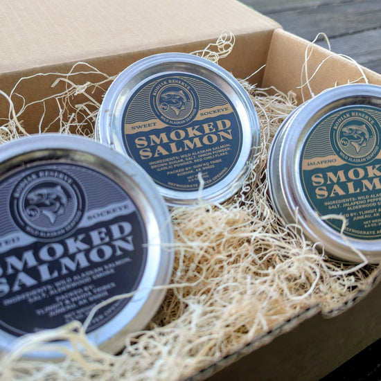 Three tins of smoked salmon in a cardboard box with decorative Aspen