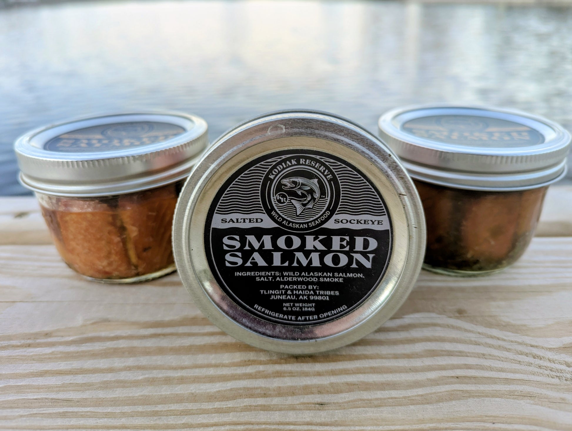 3 jars of salmon on a dock in front of water